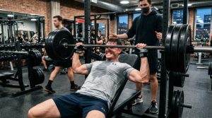 A man wearing a light grey sweat-resistant gym t-shirt during an intense weightlifting session in a modern gym