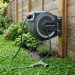 Person neatly winding a green garden hose onto a wall-mounted retractable reel.