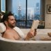 Man relaxing in a modern New York bathtub using a luxury bath pillow.